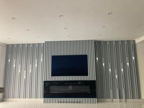 Szara ściana dekoracyjna z pionowymi panelami, podświetleniem LED, telewizorem i czarnym kominkiem elektrycznym, widok z dołu.