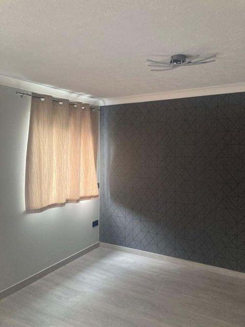 Pusty pokój po remoncie: szara ściana z geometrycznym wzorem, jasna podłoga i okno z beżową zasłoną, nowoczesna lampa sufitowa.