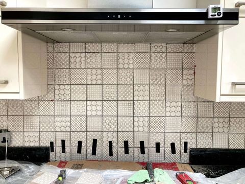 Montaż płytek dekoracyjnych w kuchni, widoczne czarne kliny dystansowe pod płytkami, okap kuchenny z timerem, fragment szafki.