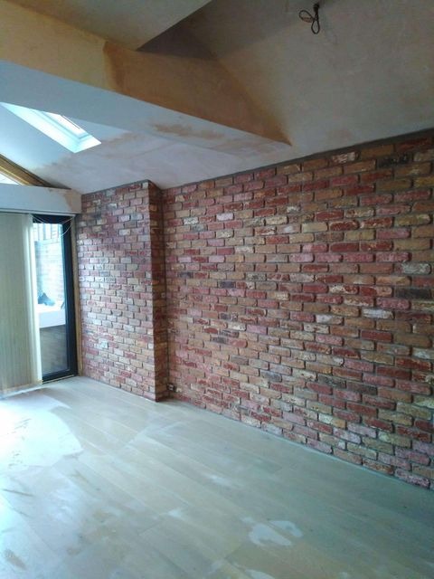 Wnętrze w trakcie prac wykończeniowych: ściana z czerwonej cegły z fugami, jasna drewniana podłoga zabezpieczona folią, surowy sufit z oknem dachowym.