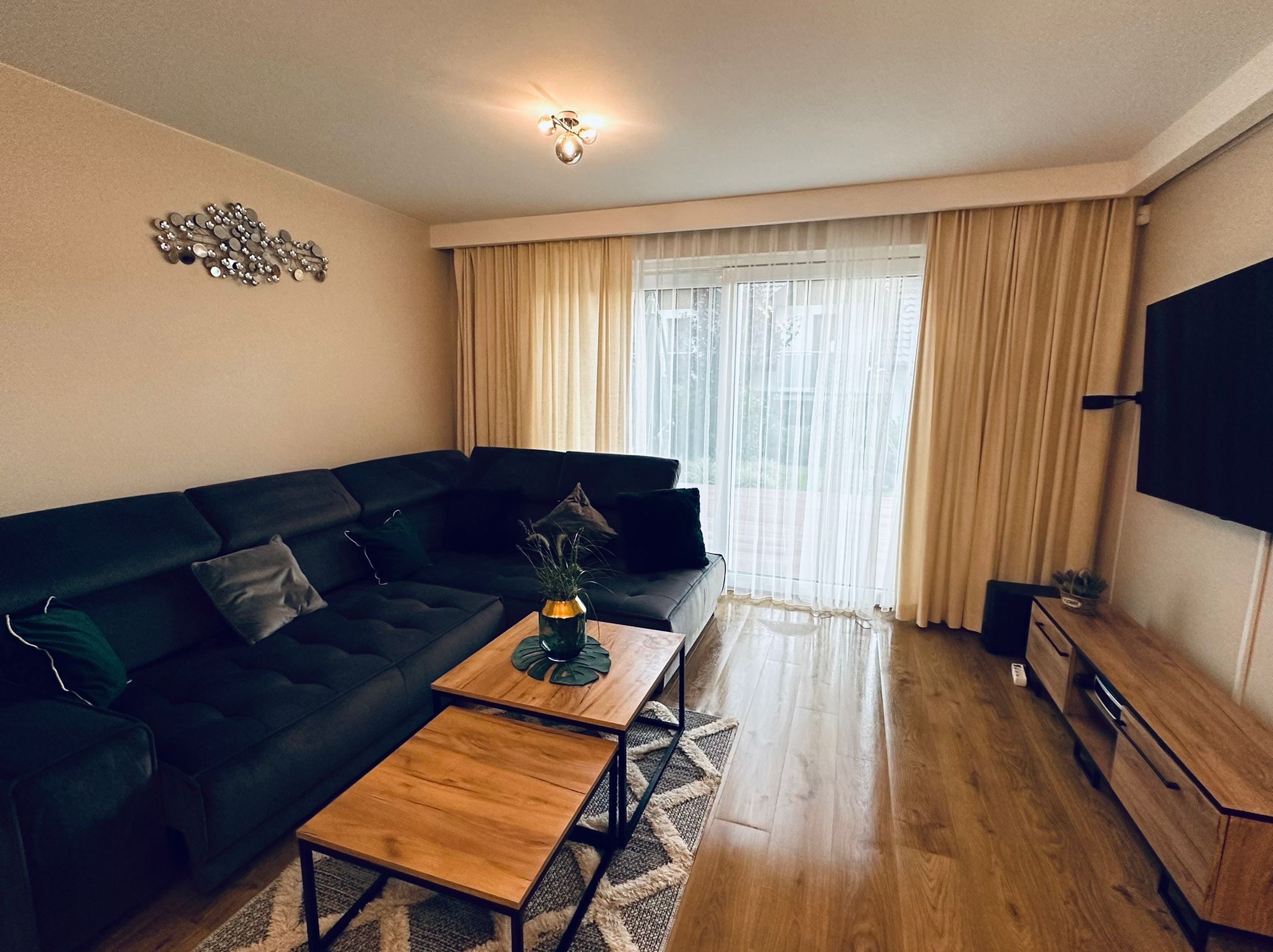 Salon z ciemnoszarą sofą narożną, drewnianymi stolikami kawowymi na metalowych nogach, parkietem i dekoracją ścienną z metalowych kółek.