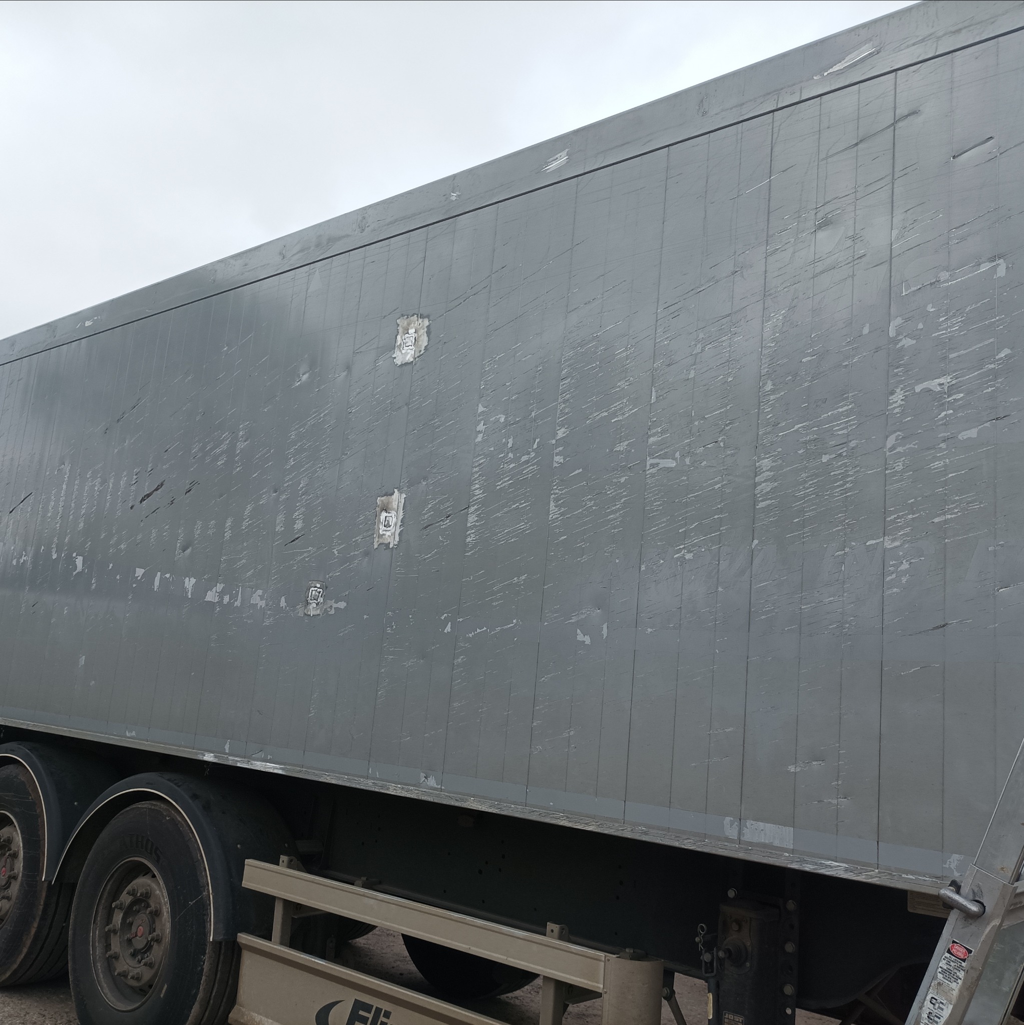Szara, boczna ściana naczepy samochodu ciężarowego w Barszczówce, z widocznymi śladami korozji i odpryskami farby, wymagająca odświeżenia i zabezpieczenia.