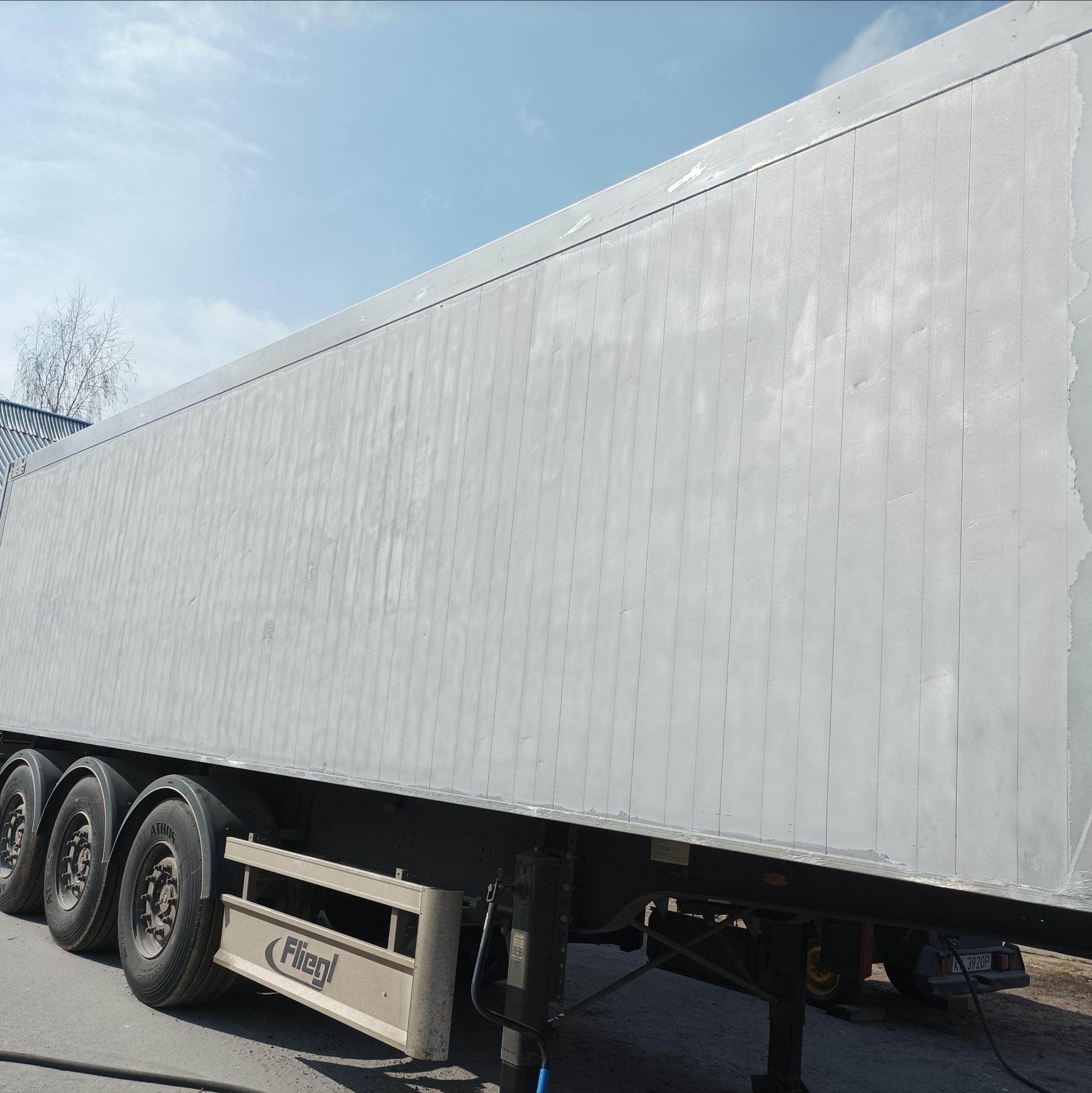 Przyczepa ciężarowa po piaskowaniu, widoczne ślady po procesie na panelach bocznych, z logo Fliegl na osłonie.
