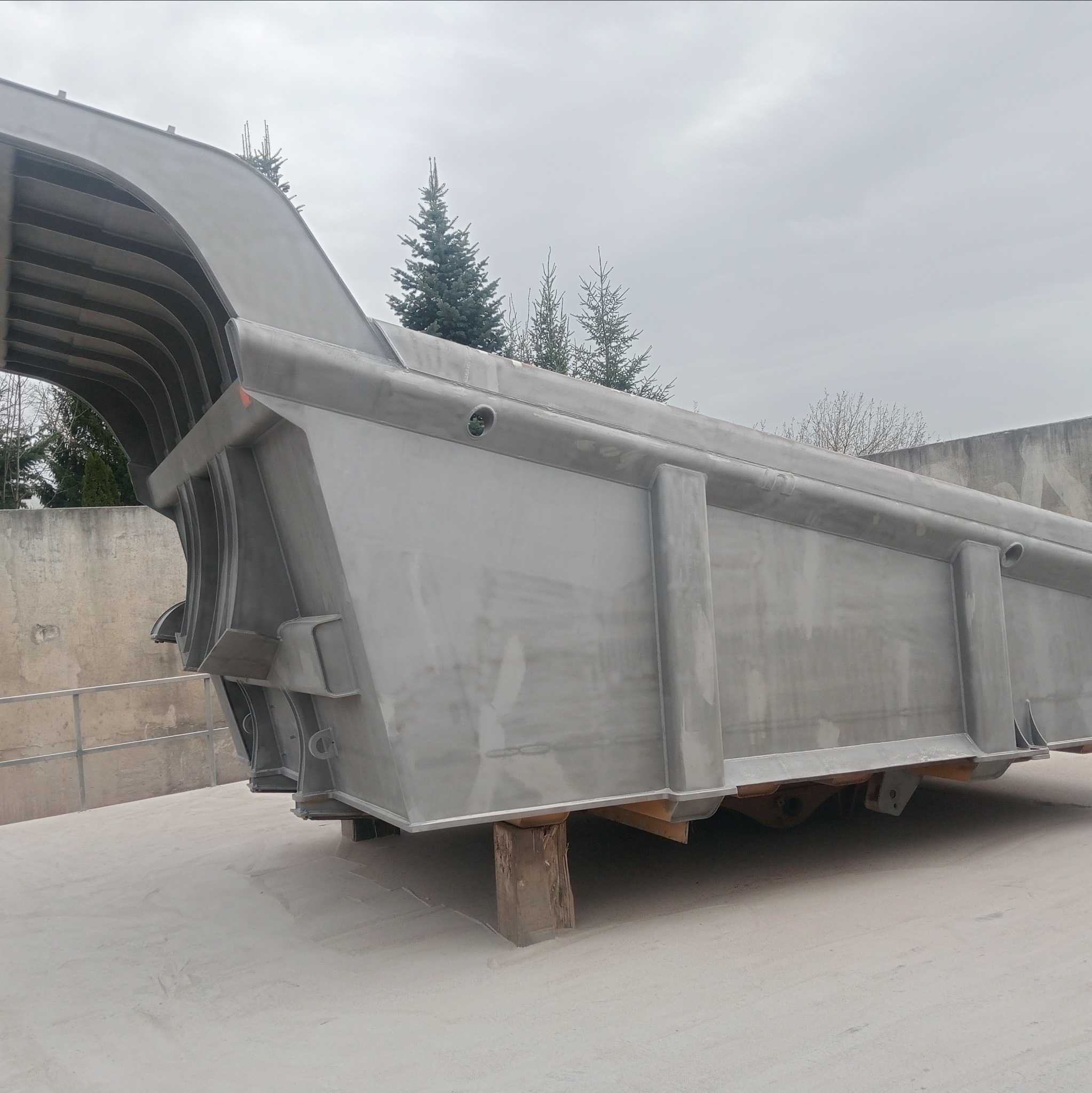 Duży, metalowy element konstrukcyjny po obróbce, prawdopodobnie po piaskowaniu, ustawiony na drewnianych podporach na betonowej powierzchni, z widocznymi elementami konstrukcyjnymi w tle.