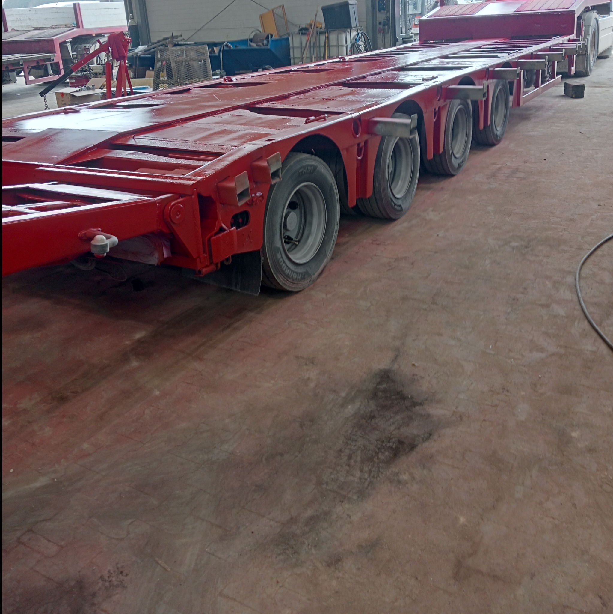Czerwona, niskopodwoziowa naczepa transportowa z wieloma osiami, świeżo po lakierowaniu, stojąca w hali.