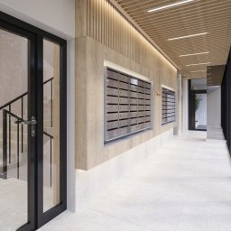 Eindom - nieruchomości - Łódź - Korytarz z drewnianą boazerią i skrzynkami pocztowymi w nowoczesnym budynku w Łodzi. Widoczne schody i drzwi z czarnymi ramami.