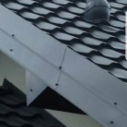 Dachpok - Ciemnoszara dachówka ceramiczna z kominkiem wentylacyjnym i obróbką blacharską w kolorze szarym, widok z dołu.