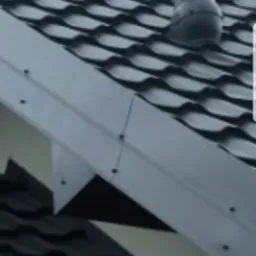 Ciemnoszara dachówka ceramiczna z kominkiem wentylacyjnym i obróbką blacharską w kolorze szarym, widok z dołu.