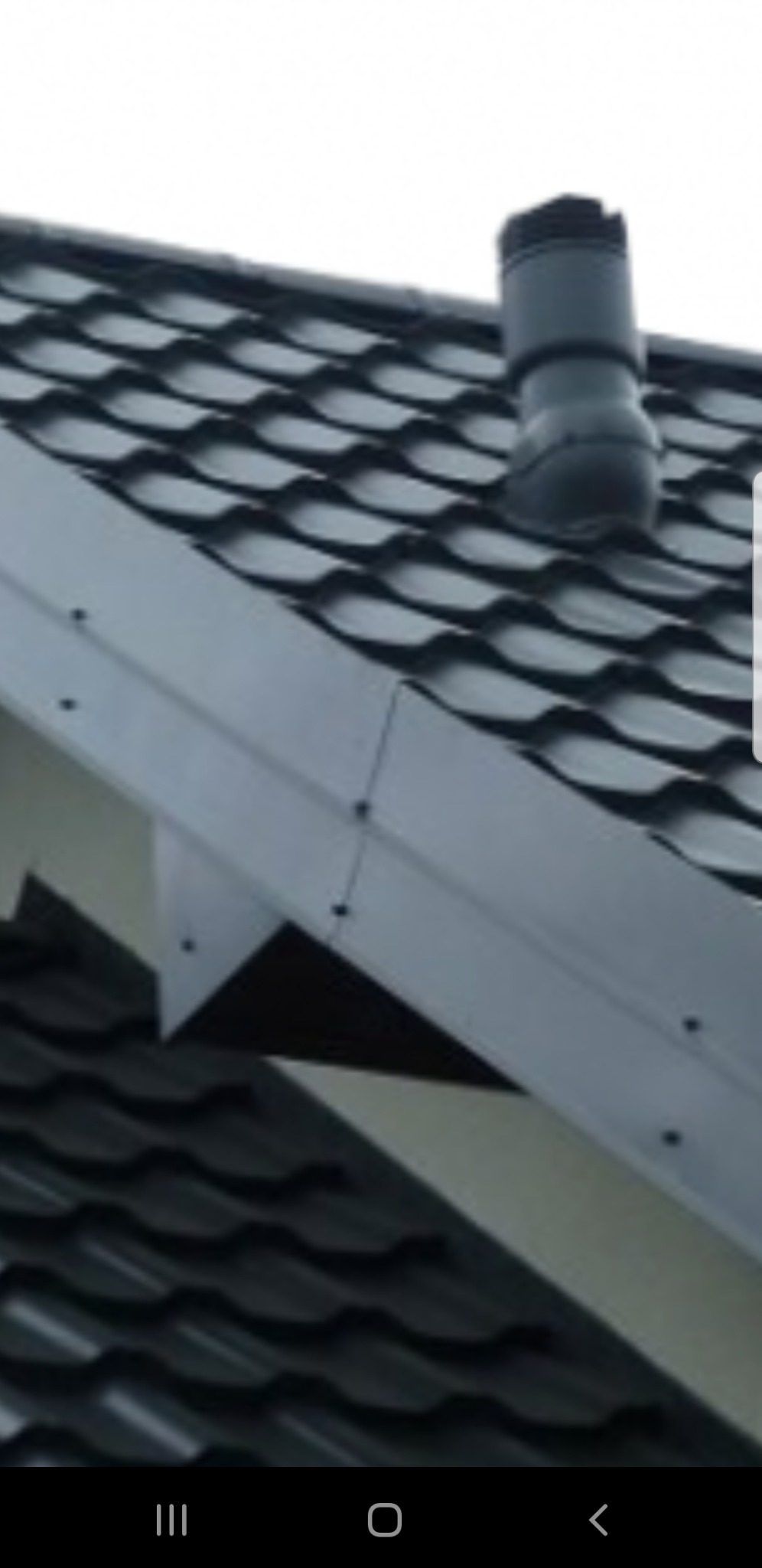 Ciemnoszara dachówka ceramiczna z kominkiem wentylacyjnym i obróbką blacharską w kolorze szarym, widok z dołu.