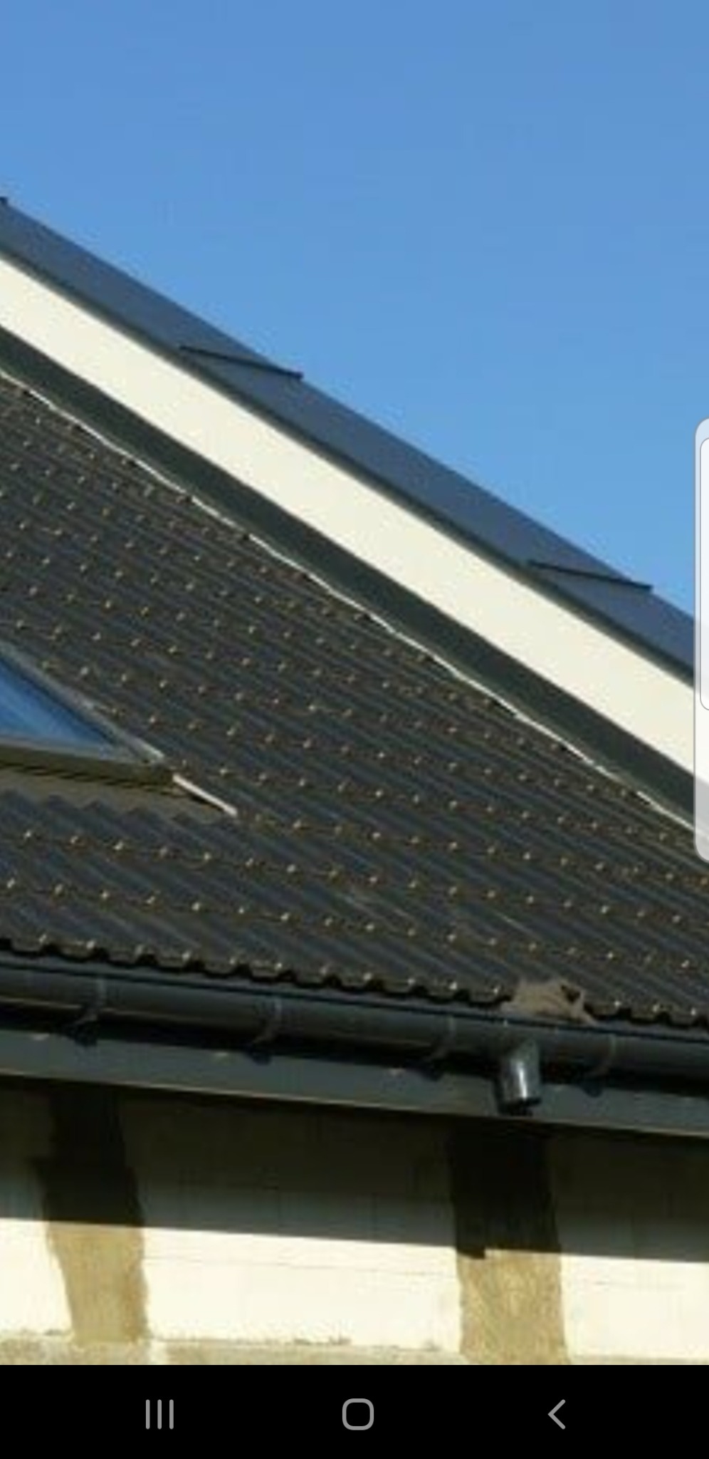 Grafitowy dach z dachówki ceramicznej z oknem dachowym i rynnami w kolorze grafitowym na tle błękitnego nieba.