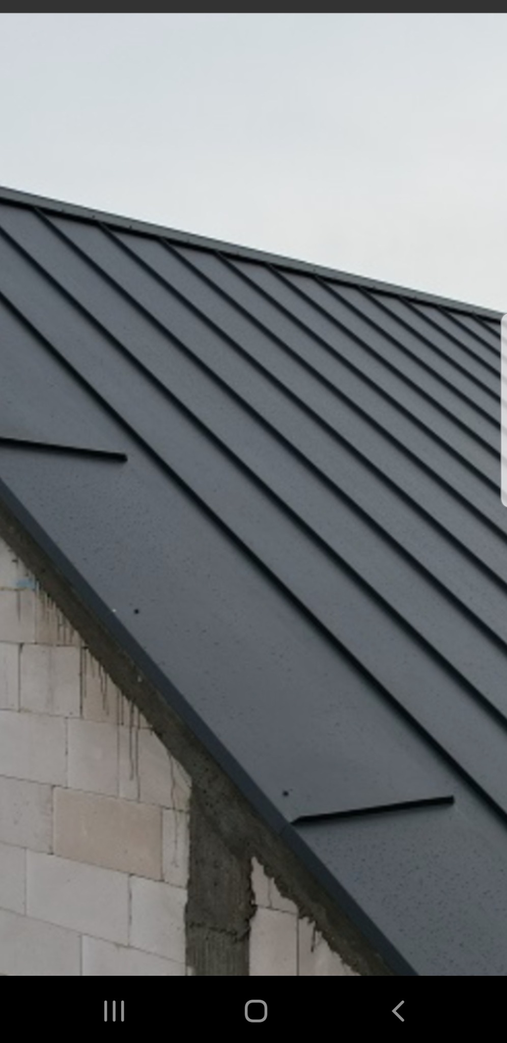 Szary dach z blachy na budynku z białego pustaka, widoczne ślady zaprawy murarskiej.