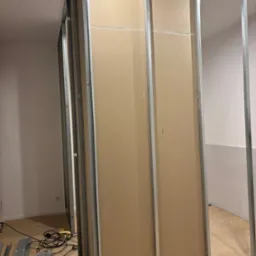 Montaż ścianki działowej z płyt gipsowo-kartonowych na metalowym stelażu w mieszkaniu w Poznaniu, widoczne narzędzia i elementy konstrukcyjne.