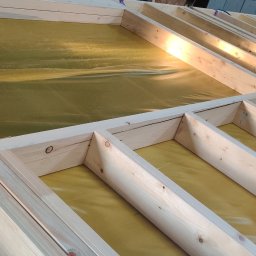 DEWERIS HOLDING PROSTA SPÓŁKA AKCYJNA - Wewnętrzna konstrukcja szkieletowa domu w trakcie budowy w Warszawie, pokryta żółtą folią izolacyjną.