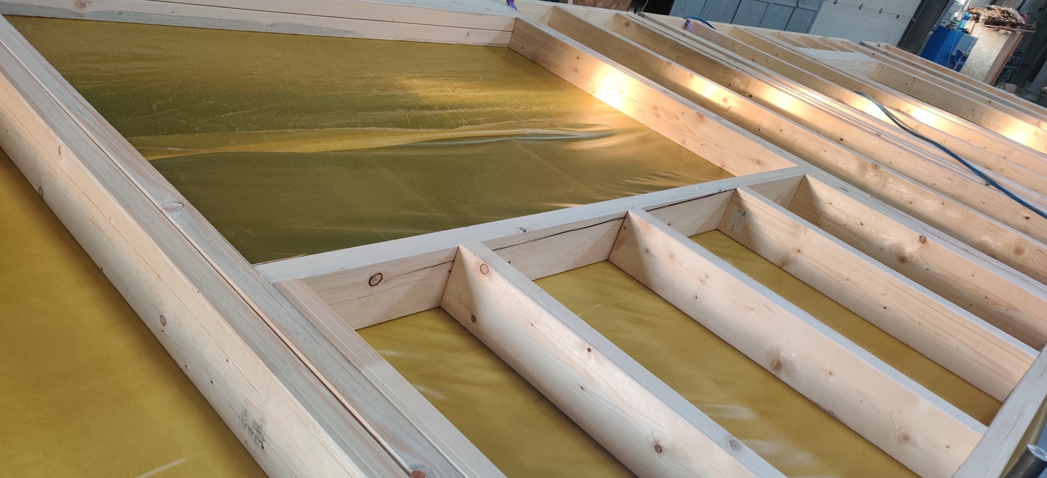 Wewnętrzna konstrukcja szkieletowa domu w trakcie budowy w Warszawie, pokryta żółtą folią izolacyjną.