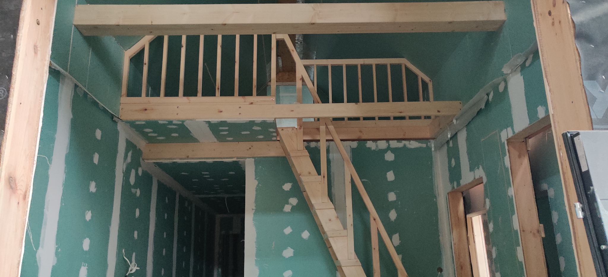 Wnętrze w trakcie rozbudowy z widoczną drewnianą konstrukcją antresoli ze schodami i barierką, ściany pokryte płytami gipsowo-kartonowymi przed szpachlowaniem.