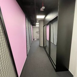 Serhii Hubrii SH ART - Długi korytarz z szafami przesuwnymi o czarnych ramach, różowymi ścianami i czarną podłogą, widoczna drabina i puszki z farbą w oddali.