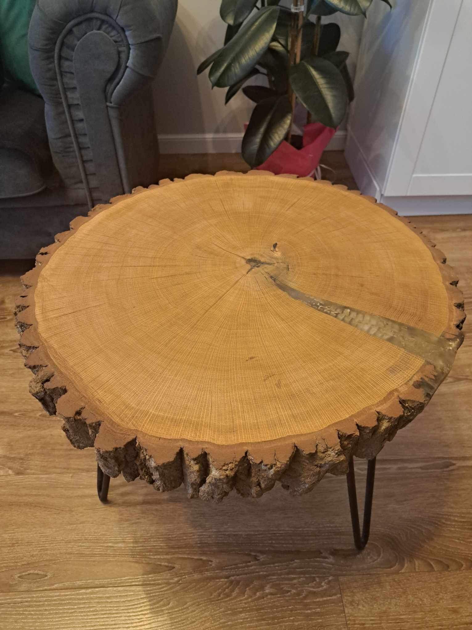 Stolik kawowy z blatem z plastra drewna z żywicą epoksydową, metalowe nogi, w tle szara sofa i roślina doniczkowa.