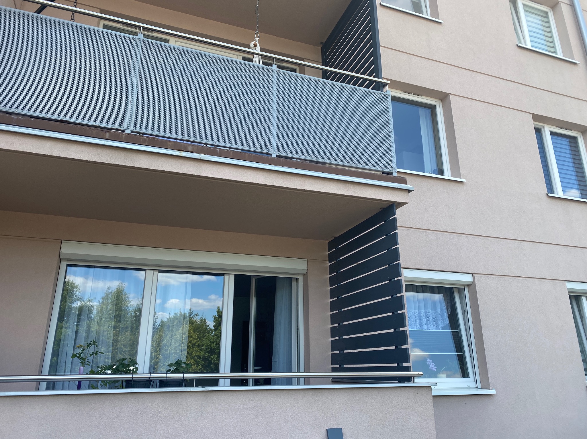 Balkony w bloku z metalową ażurową balustradą i drewnianymi panelami bocznymi, widok z dołu.