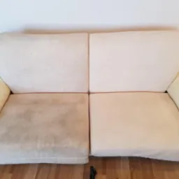 Dwusiedziskowa kanapa w odcieniach beżu, ukazująca efekt czyszczenia tapicerki: po lewej stronie widoczny brudny, wyblakły materiał, po prawej - czysta, odświeżona powierzchnia.