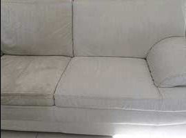 Widok z przodu białej kanapy, gdzie lewa strona jest wyraźnie brudna, a prawa po czyszczeniu, ukazując kontrast efektu prania tapicerki.