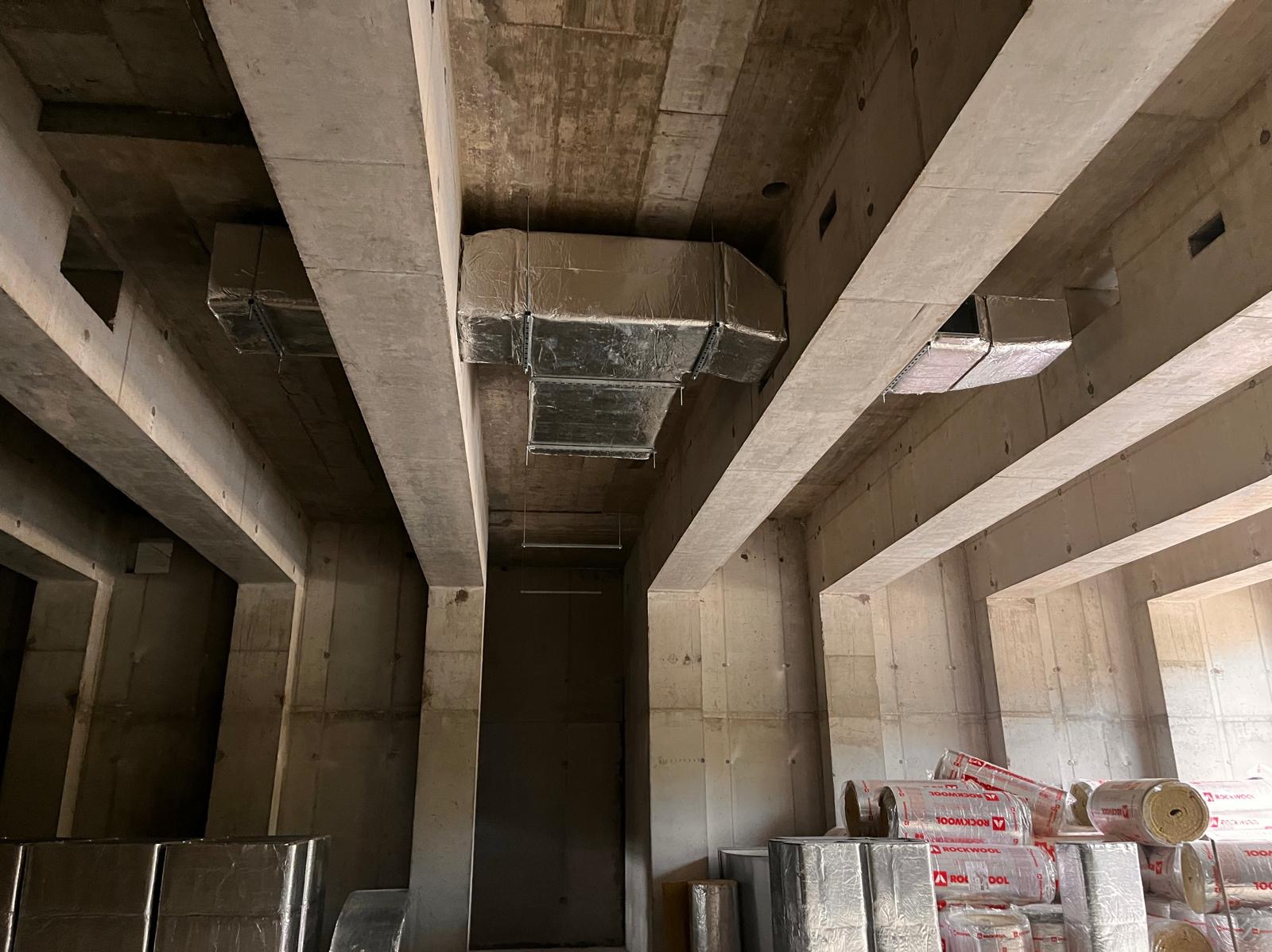 Surowy stan montażu kanałów wentylacyjnych z izolacją w nowym budynku w Zabrzu, widoczne materiały izolacyjne Rockwool. Ujęcie z dołu, podkreślające konstrukcję stropu.