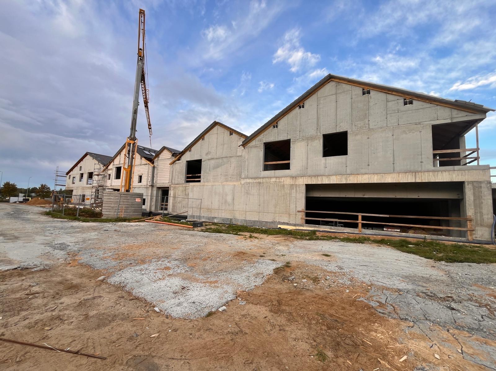 Wznoszenie szeregu domów w stanie surowym zamkniętym, widoczny dźwig budowlany i teren budowy z elementami szalunków.