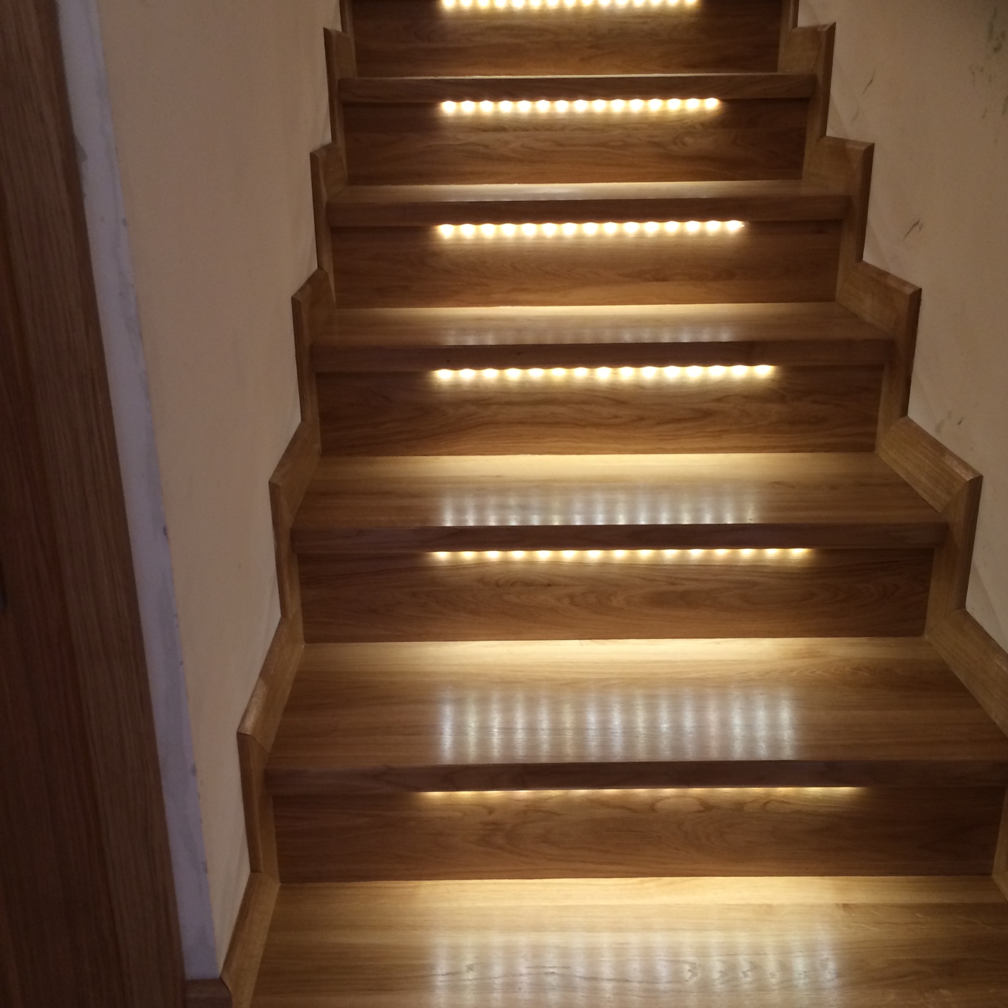 Klatka schodowa z dębowymi stopniami, podświetlona listwami LED, widok z dołu.