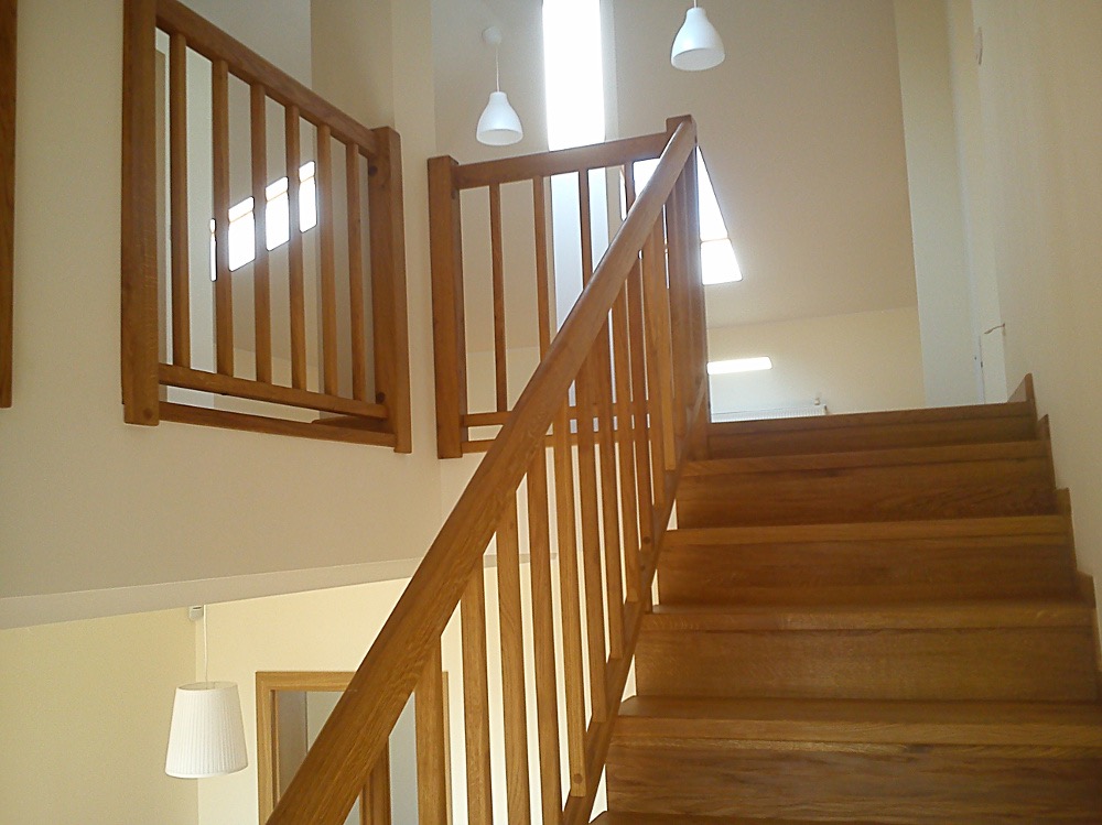 Jasne, drewniane schody z balustradą w nowoczesnym domu, widok z dołu, oświetlenie sufitowe.