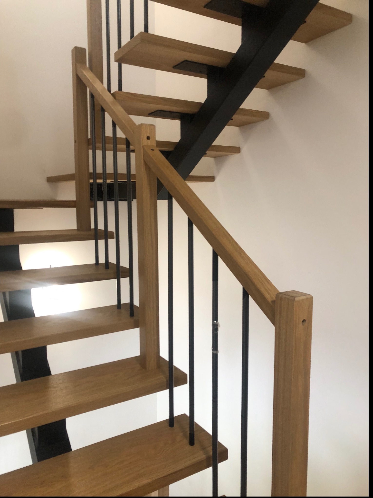 Nowoczesne schody o konstrukcji wspornikowej z drewnianymi stopniami i balustradą z drewnianymi słupkami i czarnymi, metalowymi prętami.