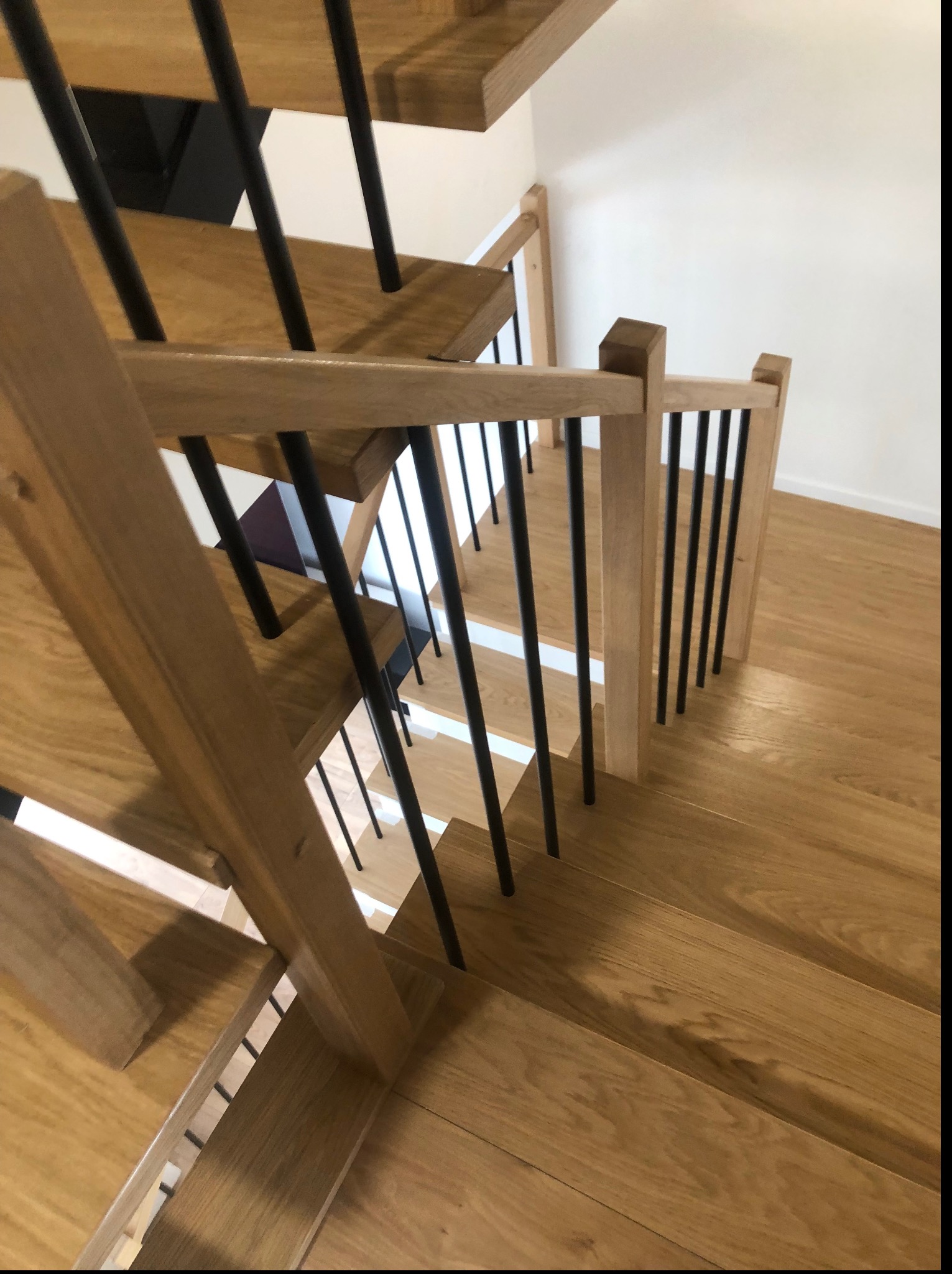 Jasne schody z drewnianymi stopniami i czarnymi, metalowymi balustradami, widok z góry, z delikatnym oświetleniem i widoczną strukturą drewna.