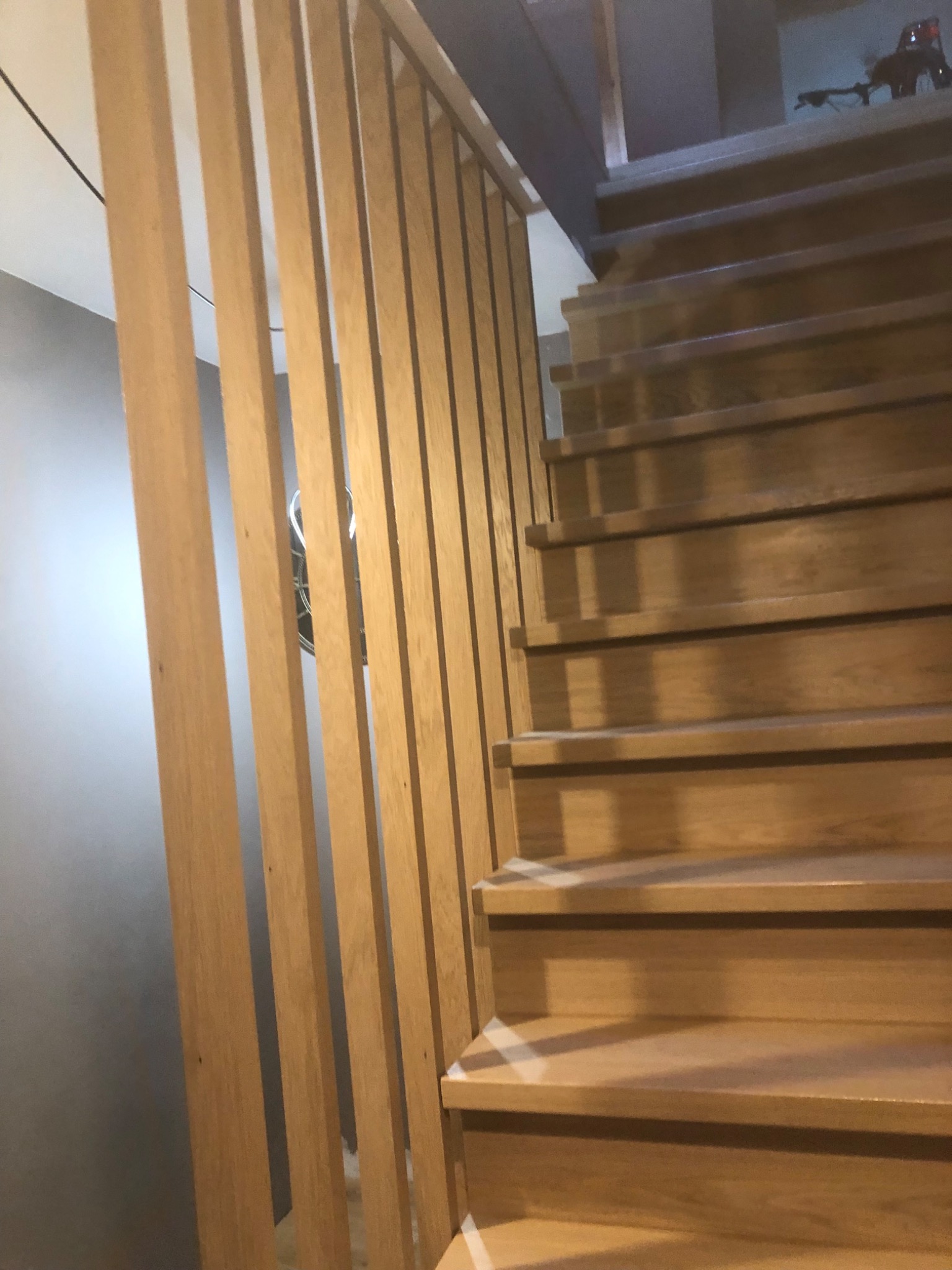 Drewniane schody z ażurową balustradą z pionowych listew. Naturalne oświetlenie podkreśla fakturę drewna. Widok z dołu, lekko z boku.