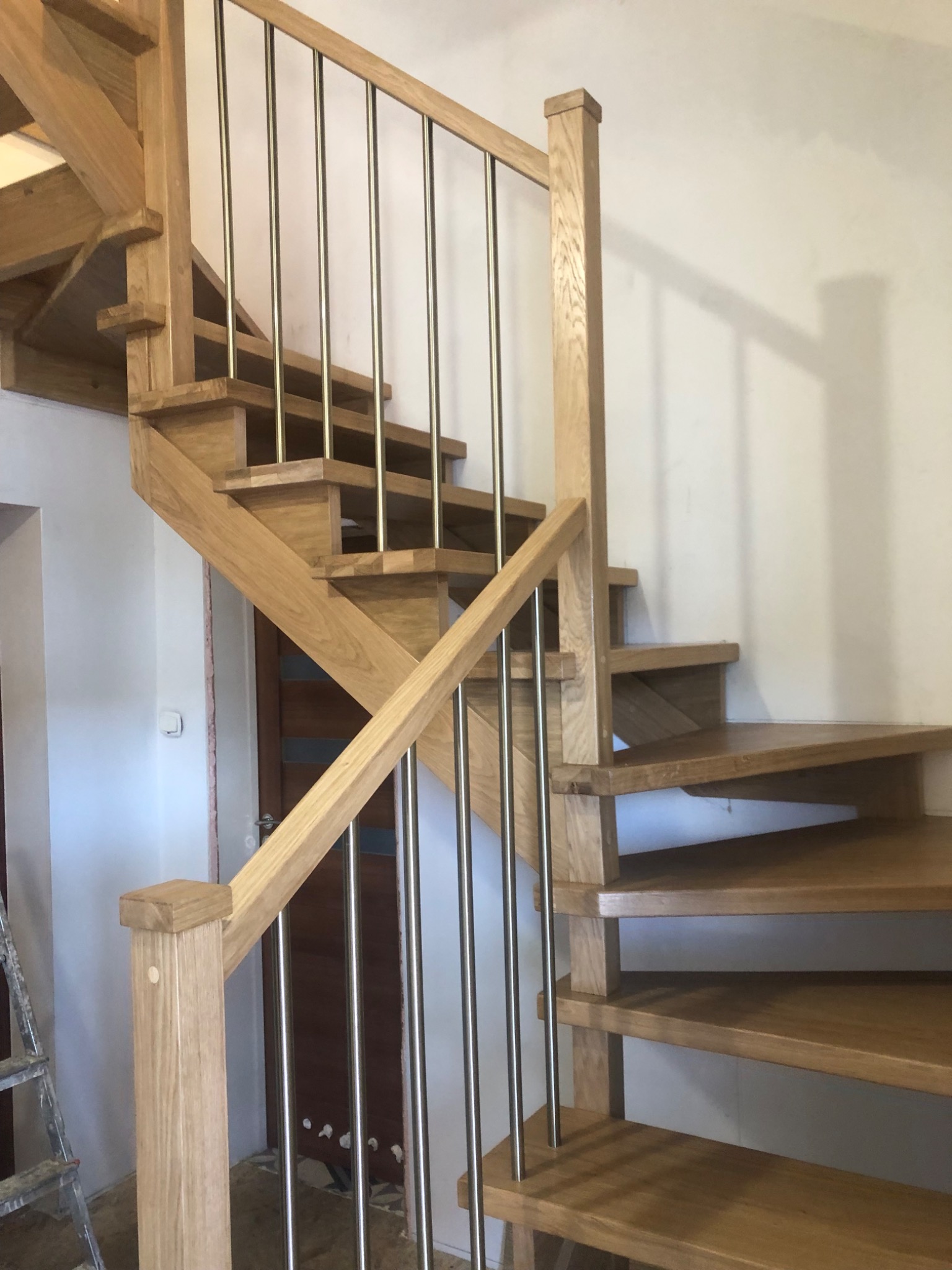 Jasne, drewniane schody z metalową balustradą w nowoczesnym wnętrzu. Widoczne detale konstrukcyjne i naturalna faktura drewna. Schody kręte z elementami zabiegowymi.