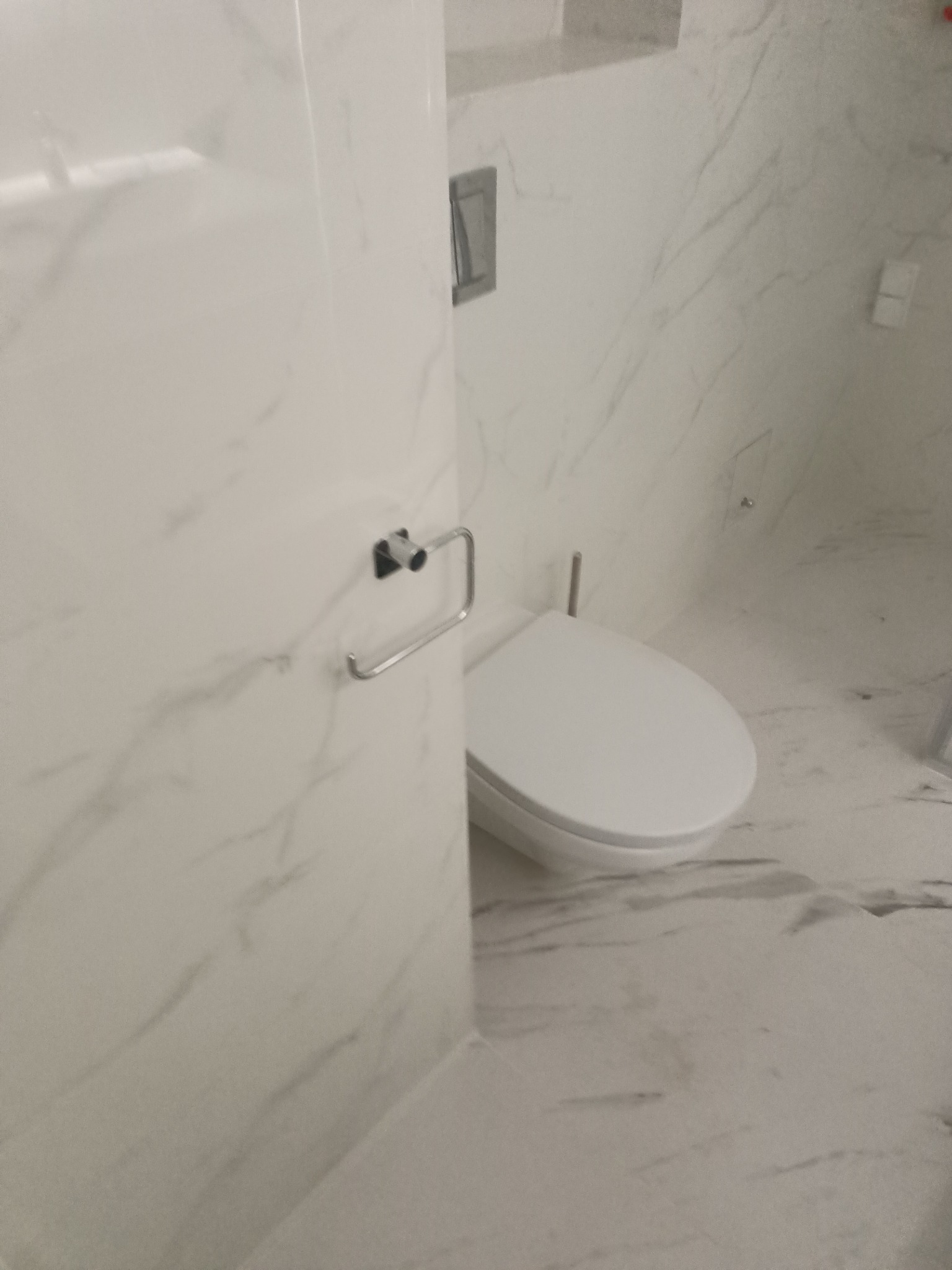 Nowoczesna łazienka wykończona białym marmurem, widoczny fragment toalety i uchwyt na papier toaletowy po lewej stronie.