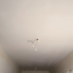 Art-Decor Mariusz Lorenc - Gładka, pomalowana na biało powierzchnia sufitu z wystającym kablem elektrycznym w miejscu planowanego oświetlenia, ściany w trakcie szpachlowania.