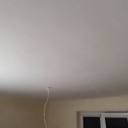 Art-Decor Mariusz Lorenc - Wnętrze po szpachlowaniu sufitu, widoczny kabel wystający z otworu, ściany przygotowane do malowania, okno w dolnej części kadru.