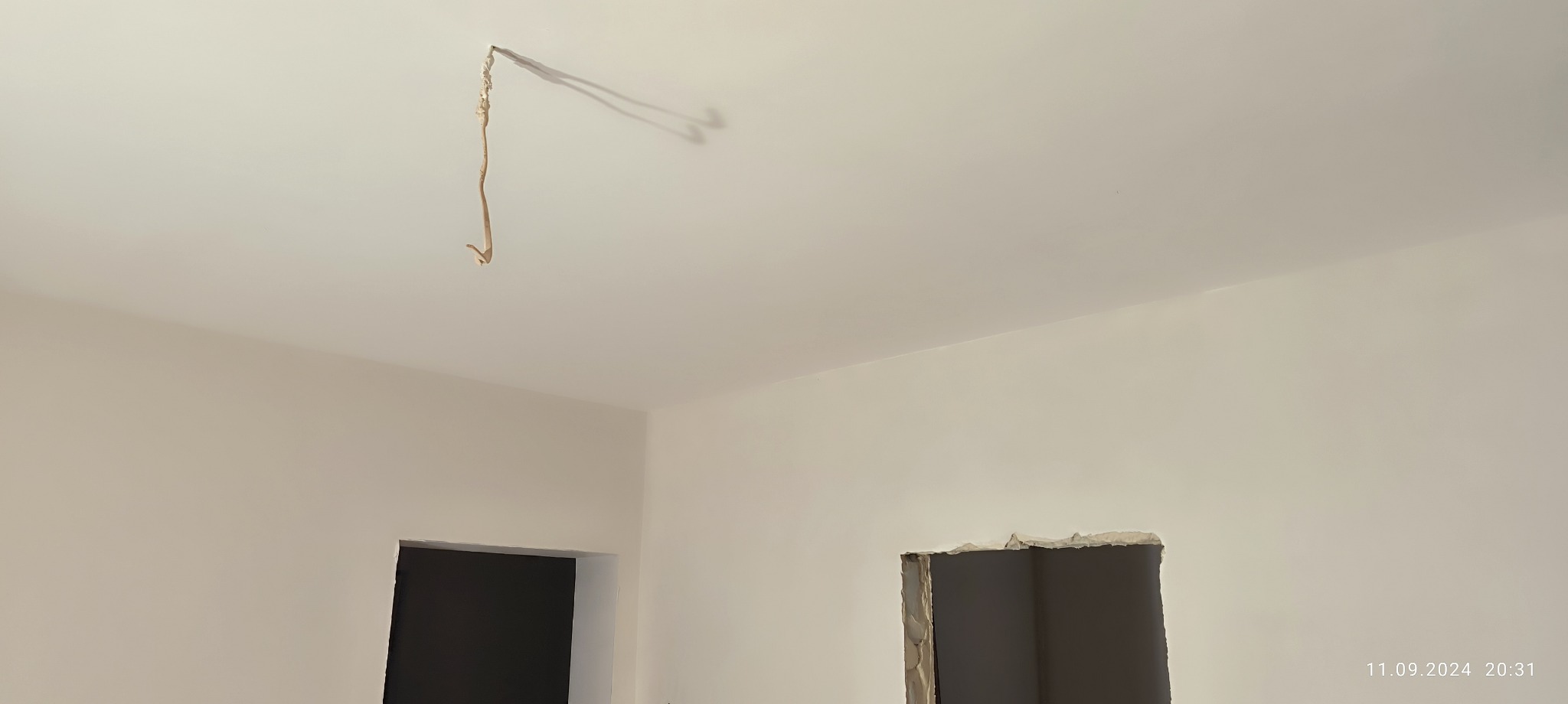 Świeżo pomalowane na biało wnętrze z widocznym kablem wystającym z sufitu i otworem w ścianie, prawdopodobnie przygotowywanym pod drzwi.