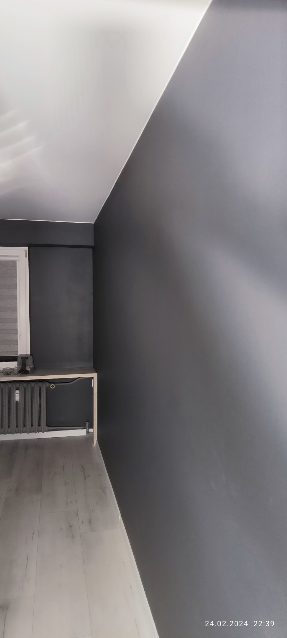 Pomieszczenie po malowaniu ścian na kolor szary, widoczny grzejnik, parapet i panele podłogowe.