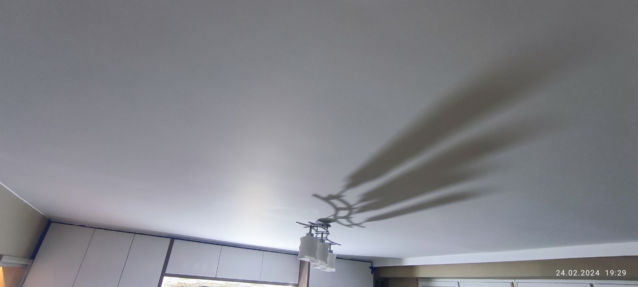 Biały, gładki sufit z widocznymi cieniami lampy wiszącej, widok z dołu.