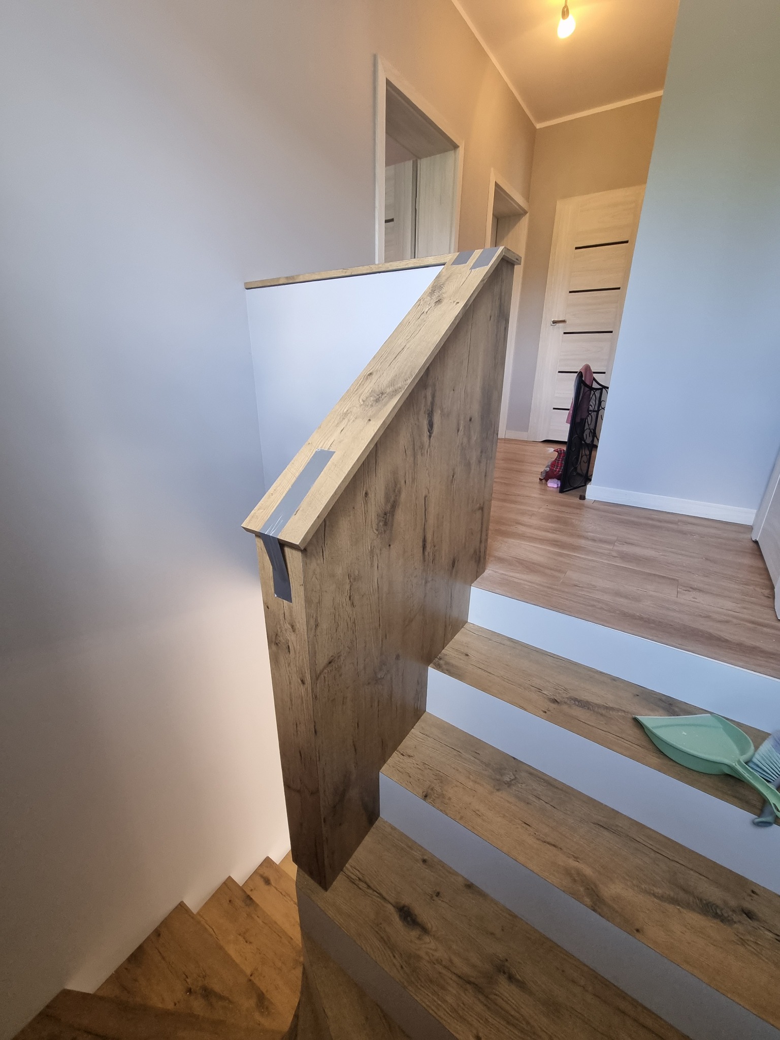 Schody drewniane z białymi podstopnicami, widok z góry, zabezpieczone taśmą malarską, w tle widoczna zamiataczka i szufelka.