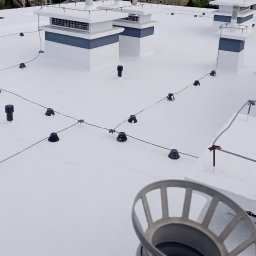 IZO PERFECT Mateusz Gardoliński - Biały dach pokryty świeżą warstwą hydroizolacji z widocznymi elementami instalacji odgromowej i kominami wentylacyjnymi.