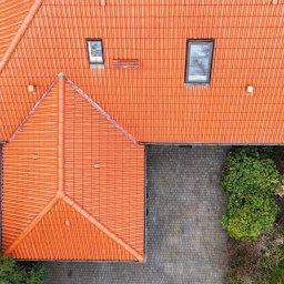 IZO PERFECT Mateusz Gardoliński - Widok z góry na dach z czerwonej dachówki ceramicznej z dwoma oknami połaciowymi, otoczony zielenią.