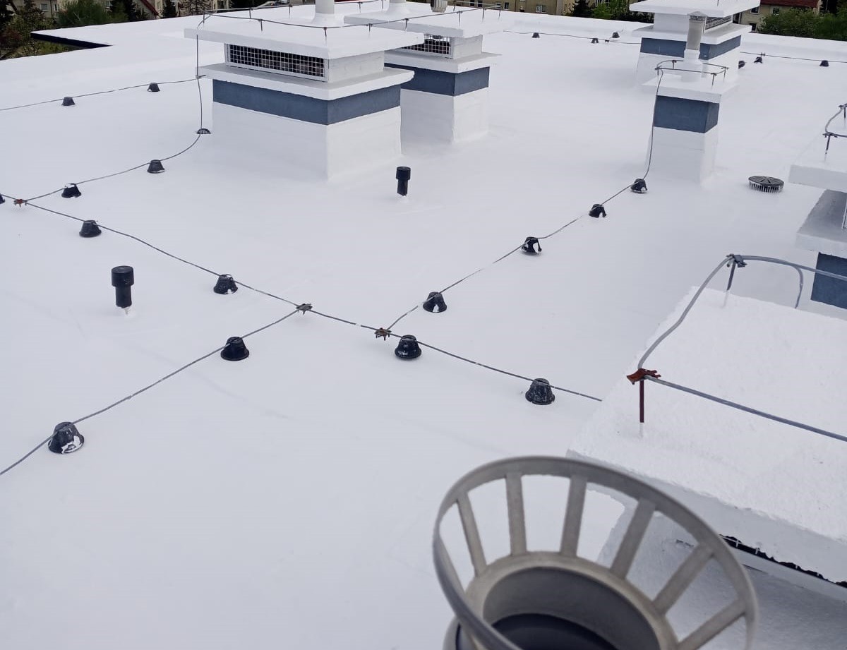 Biały dach pokryty świeżą warstwą hydroizolacji z widocznymi elementami instalacji odgromowej i kominami wentylacyjnymi.