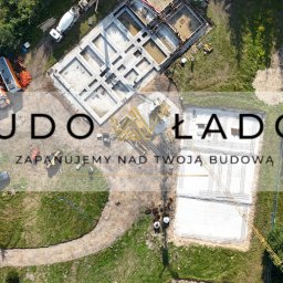 Budowładcy sp. z o.o. - Widok z lotu ptaka na dwa etapy budowy fundamentów: jeden z ułożonym szalunkiem i zbrojeniem, drugi już zalany betonem, z widoczną betoniarką, dźwigiem i zapleczem budowy na tle zieleni.