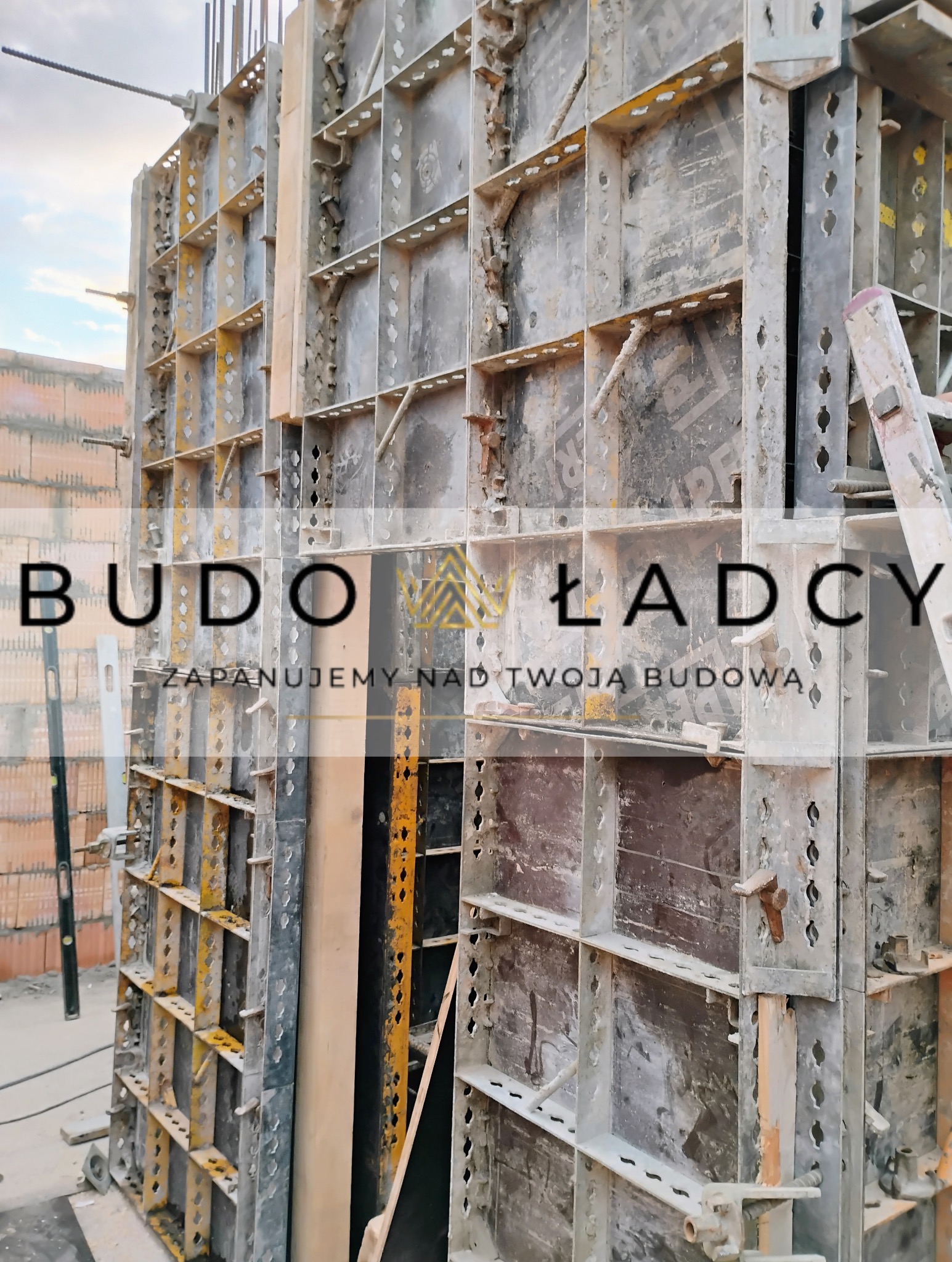 Szare szalunki do betonu na budowie domu z cegły, widoczny poziomica i drabina.