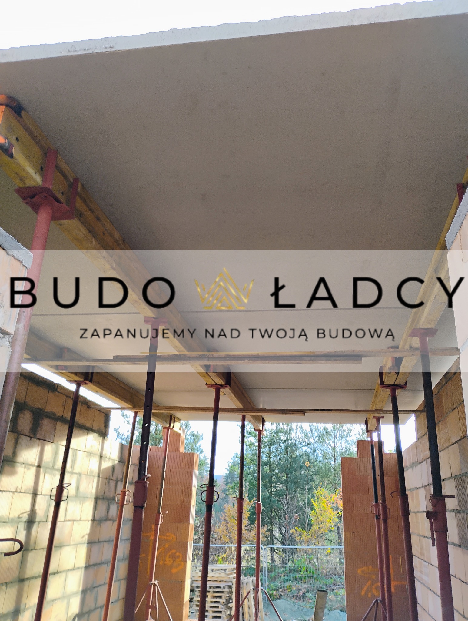 Wnętrze budynku w trakcie budowy, widoczne ściany z pustaków ceramicznych, podpory stropowe i szalunek stropu, na pierwszym planie logo firmy budowlanej.