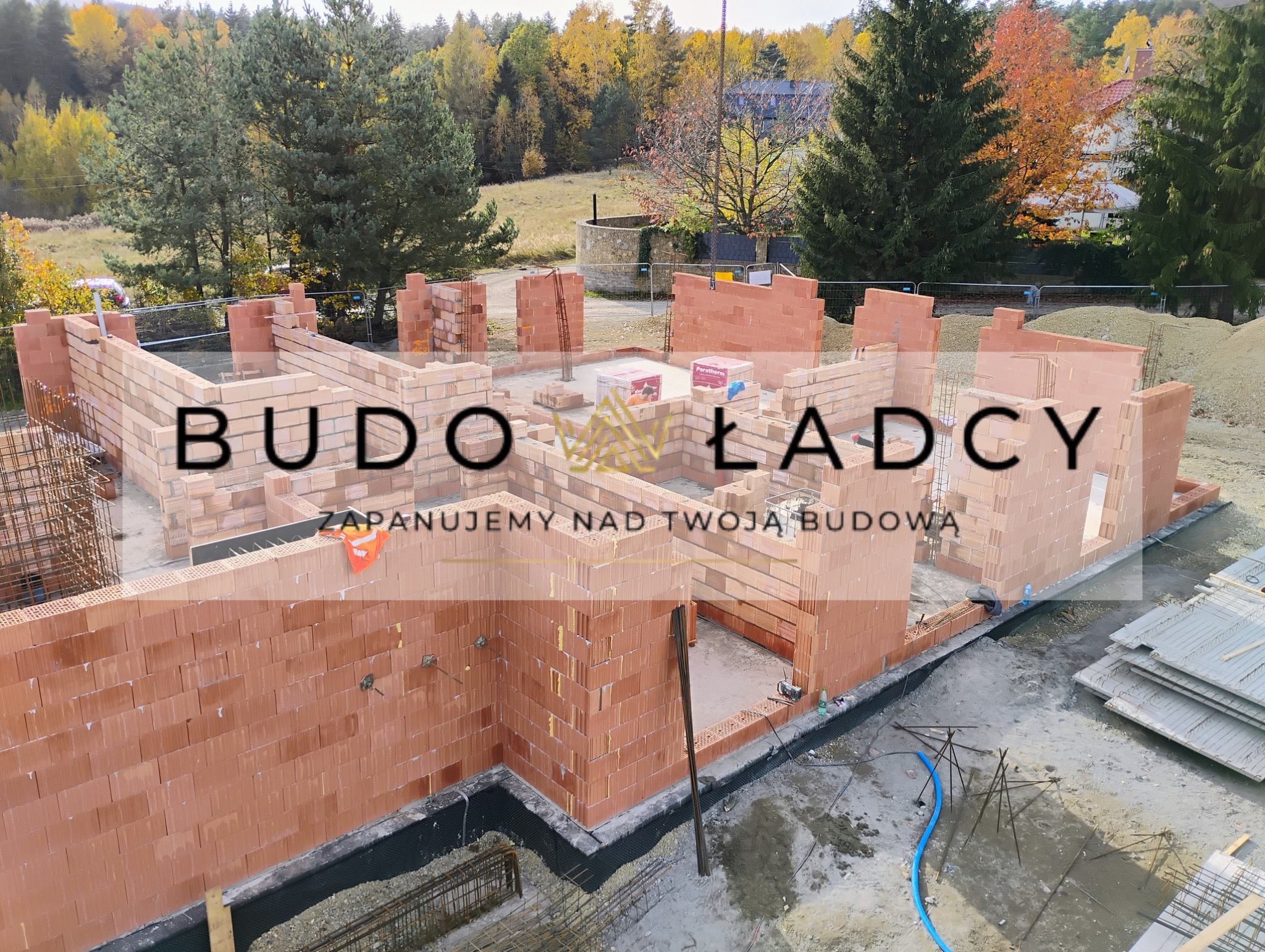 Wznoszenie murów z czerwonej cegły ceramicznej Porotherm na fundamencie domu jednorodzinnego, widok z góry, w tle jesienny krajobraz.