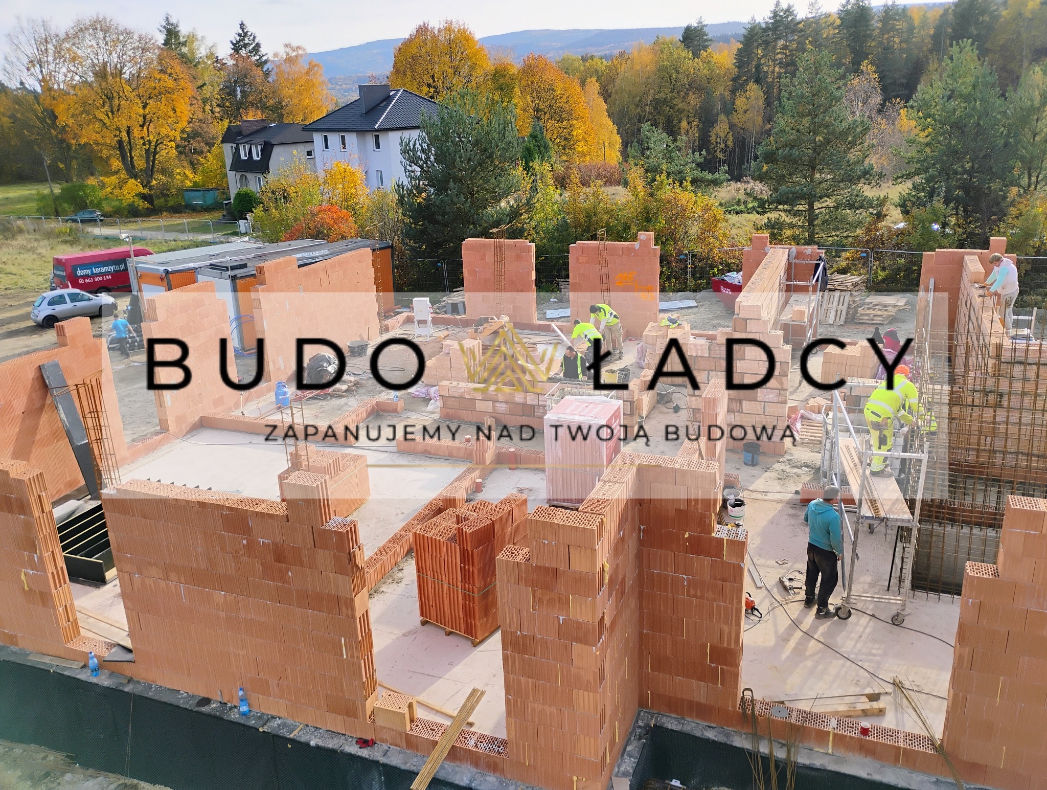 Wznoszenie ścian z czerwonej ceramiki poryzowanej na budowie domu jednorodzinnego, widok z góry, w tle jesienny krajobraz i dom mieszkalny.