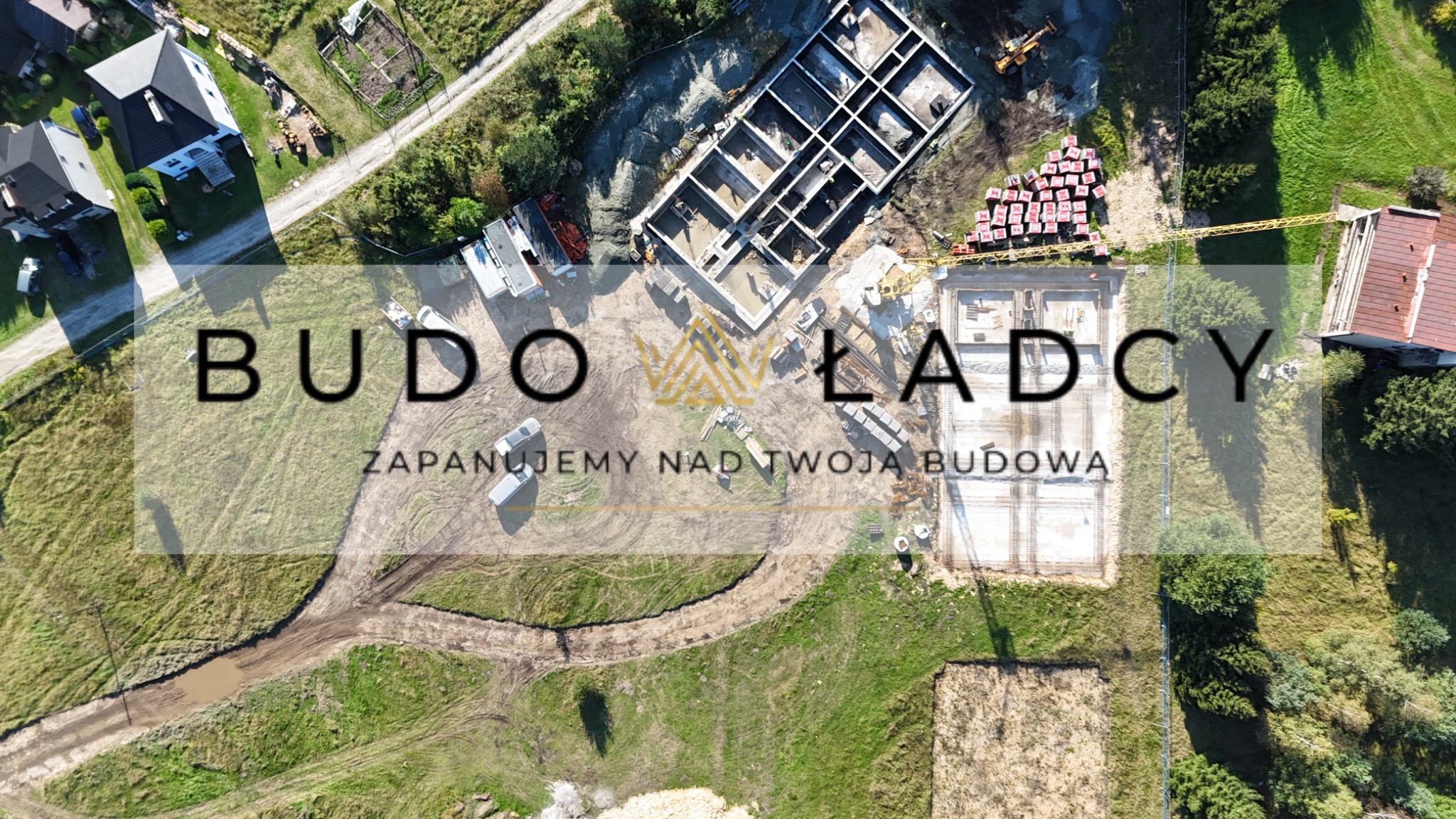 Widok z drona na plac budowy z fundamentami domu, materiałami budowlanymi i sprzętem, częściowo zasłonięty przez logo firmy Budowlańcy.