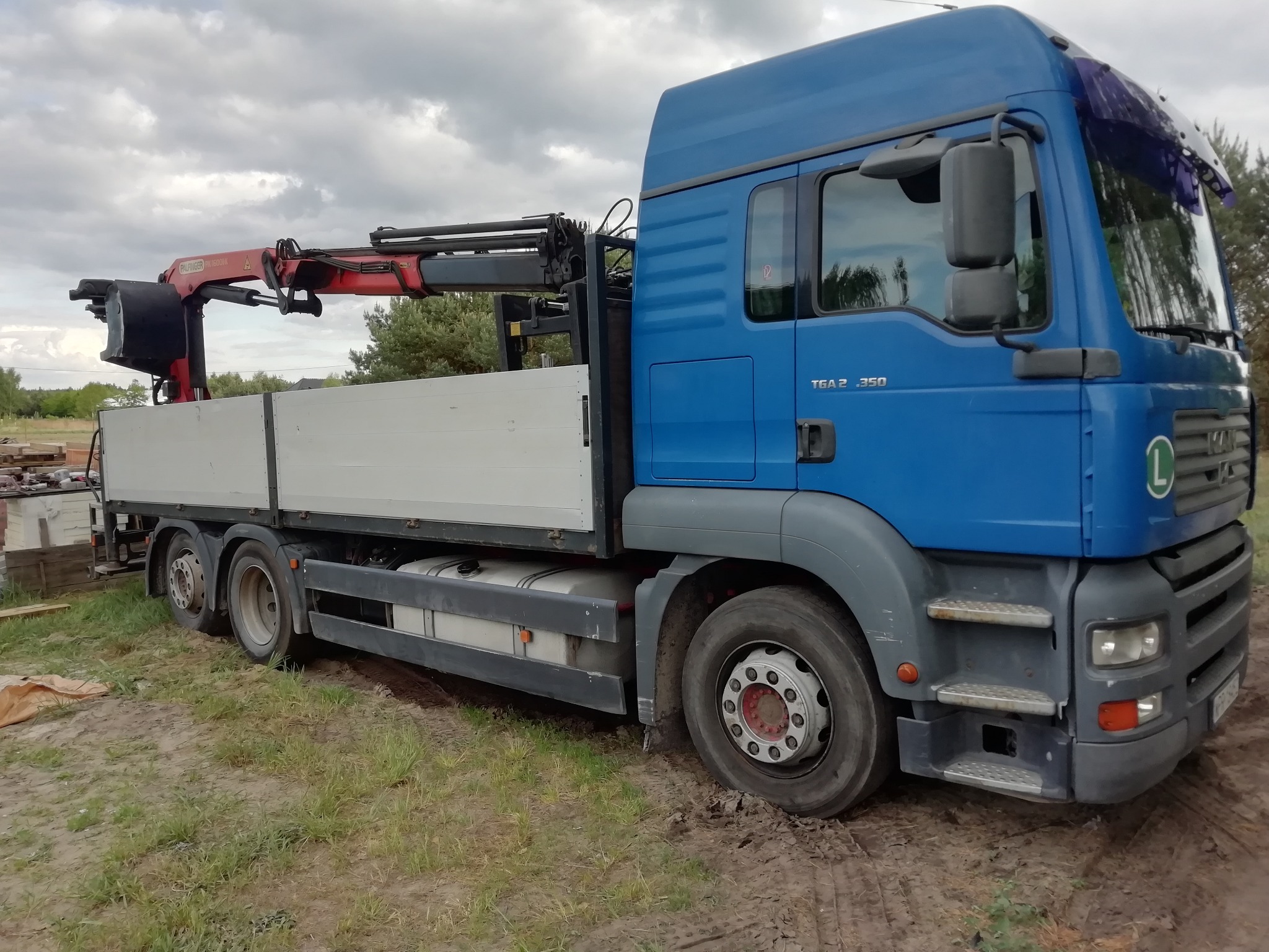 Niebieska ciężarówka MAN TGA 26.350 z zamontowanym dźwigiem Palfinger PK 16001K na platformie ładunkowej, zaparkowana na trawiastym terenie.