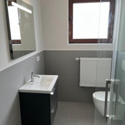 FIRMA HANDLOWO-USŁUGOWA TEMPERA WOJTCZAK PIOTR - Nowoczesna łazienka z umywalką nablatową, podświetlanym lustrem, grzejnikiem panelowym i kabiną prysznicową ze szklanymi drzwiami, wykończona szarą glazurą.